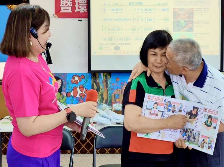 《圖說》張美阿嬤在分享生命繪本時，抱怨老公都沒說過「我愛你」，她老公連清誥當場親了她臉頰，原本大方分享的阿嬤瞬間羞紅了臉。左為長者照顧關懷協會執行長周淑玲。〈社會局提供〉